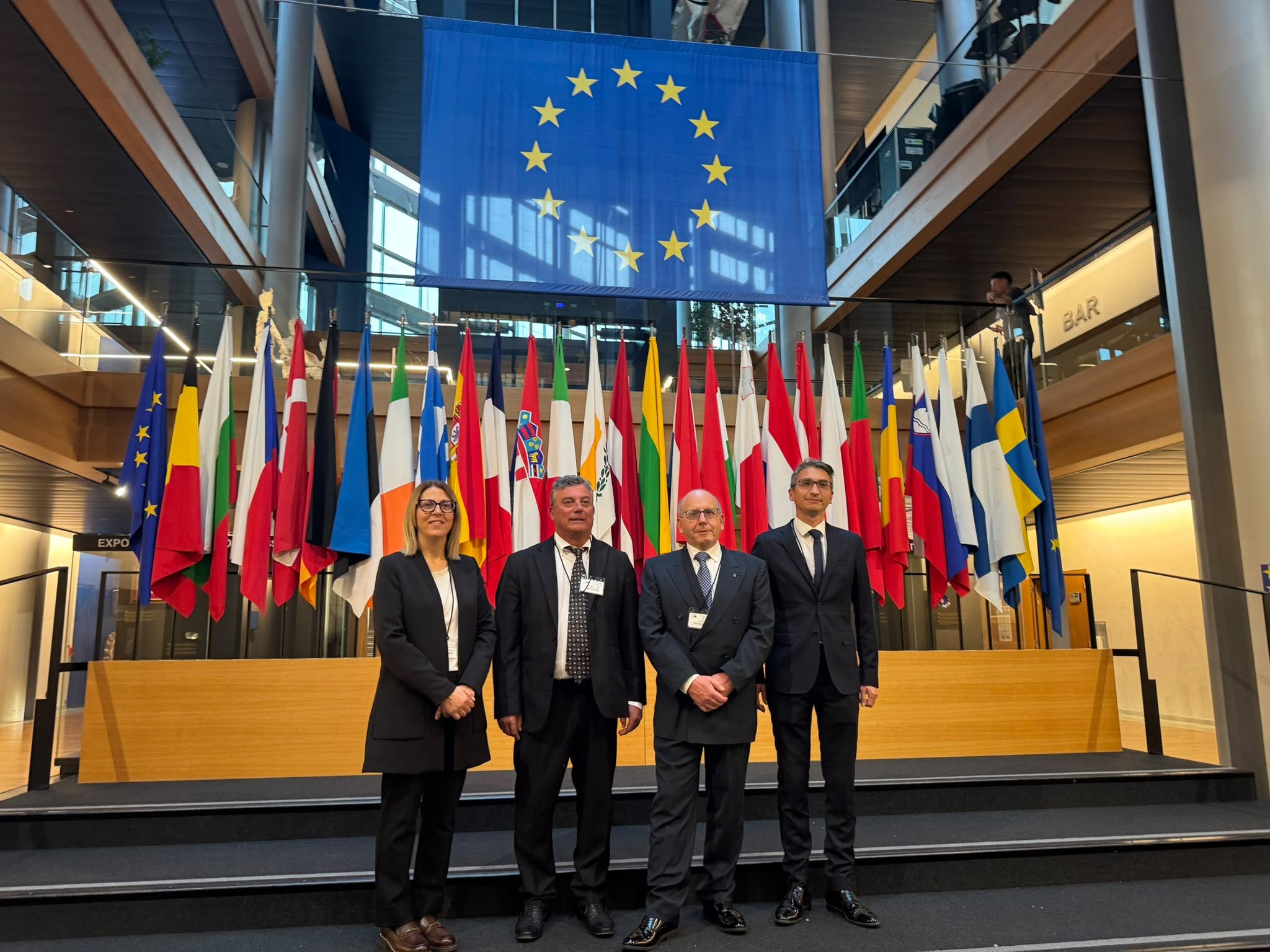 Delegazione dei rappresentanti dell’Amministrazione di Norcia in posa nella sede del Parlamento europeo, davanti alle bandiere degli Stati membri e alla bandiera dell’Unione europea